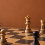 A documentary-style chess photograph in warm natural light, showing an African-designed wooden chessboard with a white rook advanced deep into a dark.