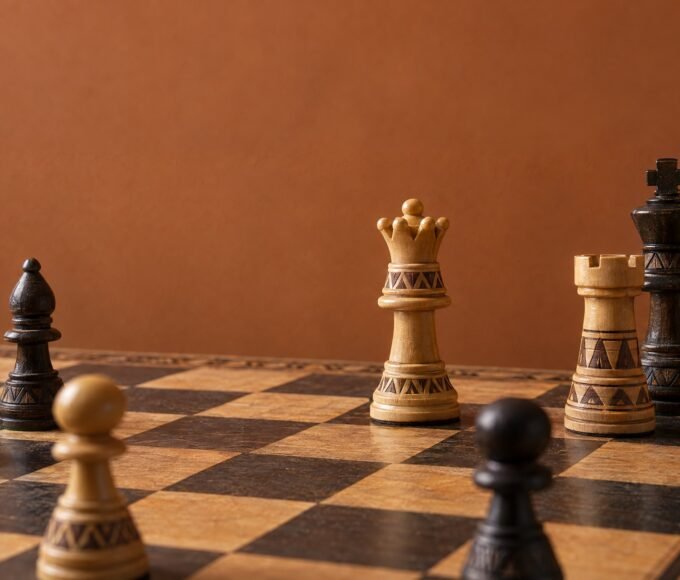 A documentary-style chess photograph in warm natural light, showing an African-designed wooden chessboard with a white rook advanced deep into a dark.