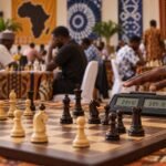 A player's hand hovers over a digital chess clock beside a tense middlegame, with the clock and pieces sharp in the foreground and a busy Nigerian.