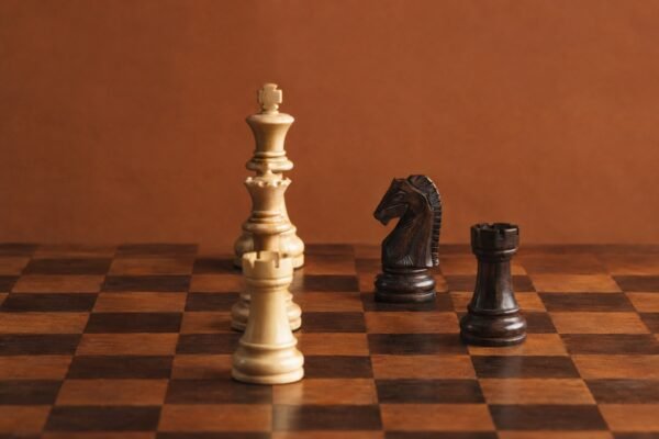 A documentary-style chess photograph in warm natural light, showing a wooden board with three white heavy pieces aligned on the c-file against a dark.