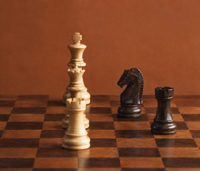 A documentary-style chess photograph in warm natural light, showing a wooden board with three white heavy pieces aligned on the c-file against a dark.