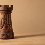 A hand-carved wooden chess rook decorated with Nok-inspired geometric carving, standing on a warm sand-coloured surface